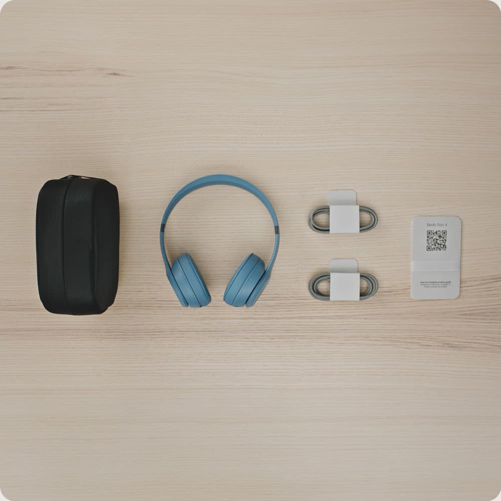 Beats Solo 4 box contents laid out: carrying case, Slate Blue headphones, two cables and the printed guide