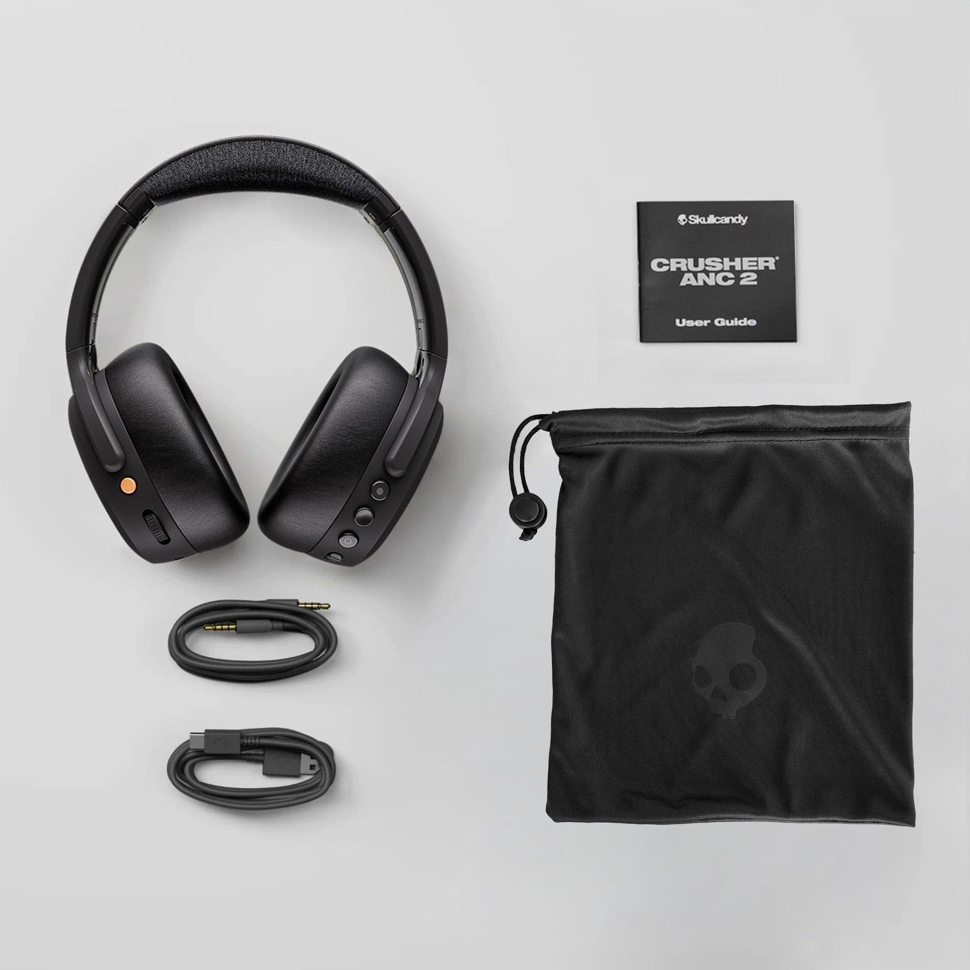 Crusher ANC 2 headphones laid out with a USB-C cable, a back-up AUX cable, a drawstring bag and the user guide